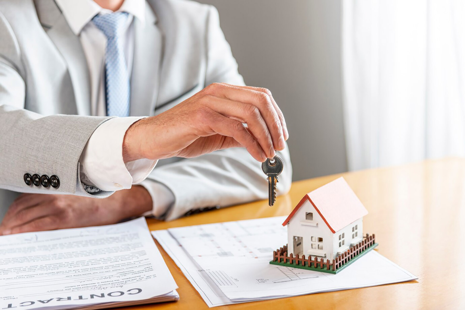 person-holding-house-keys-toy-model-house-desk_23-2148301737