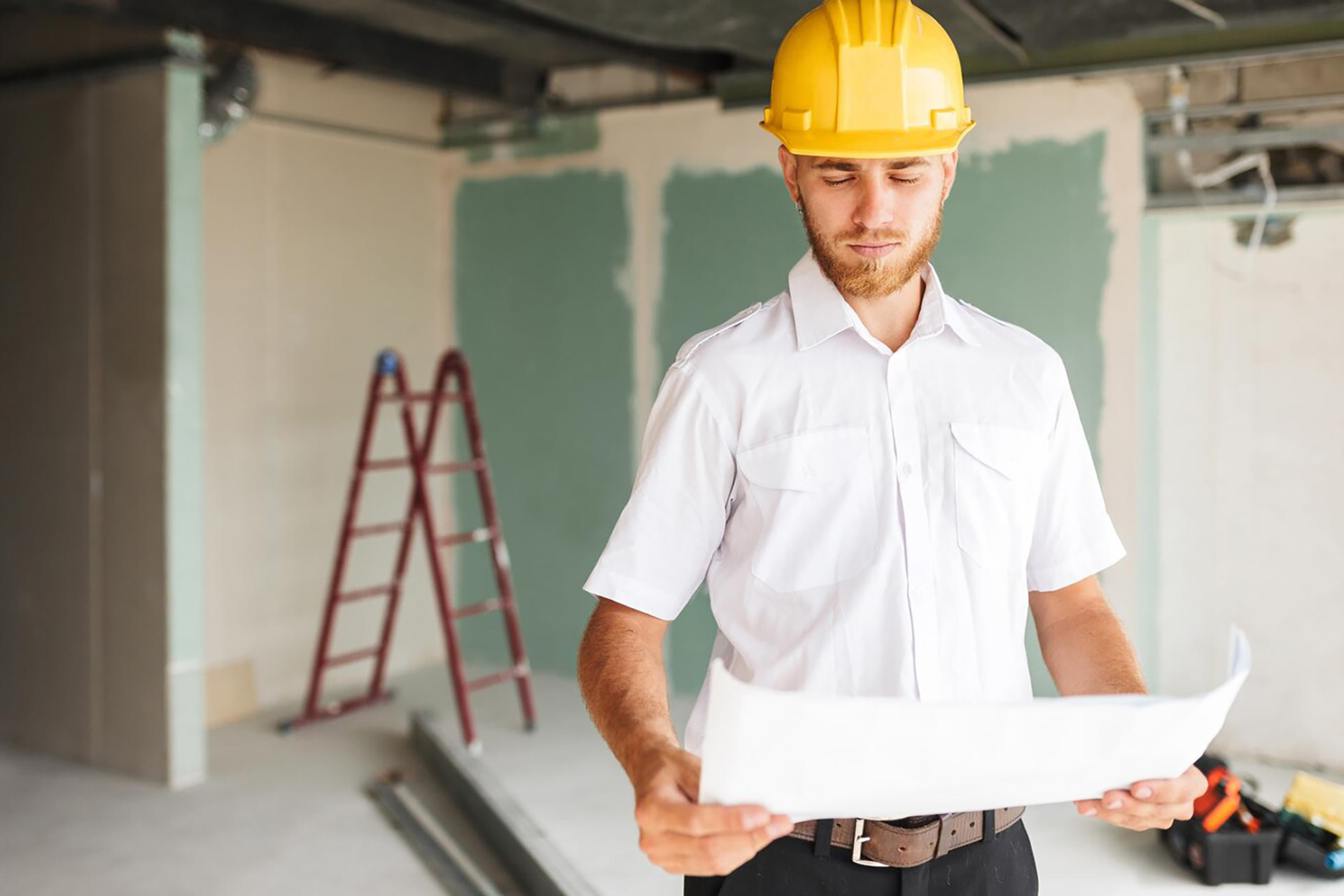 young-architect-white-shirt-yellow-hardhat-thoughtfully-looking-plan-new-apartment-with-ladder-background_574295-1584